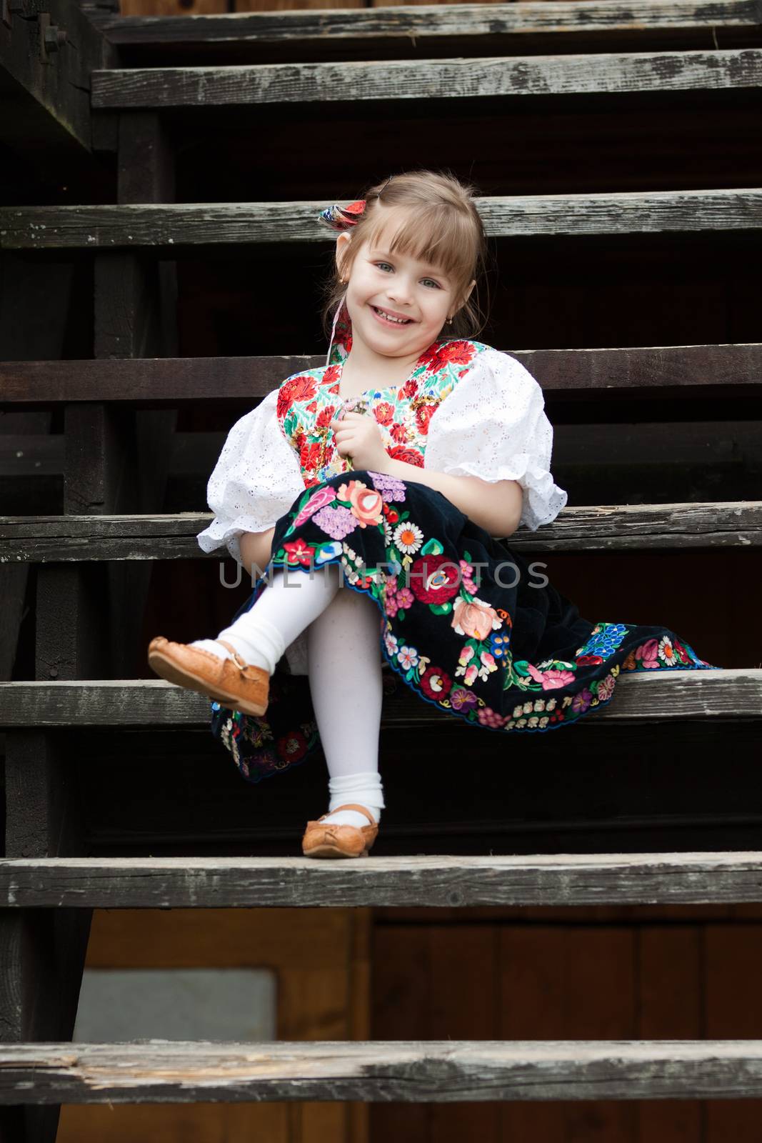 Small girl in traditional costume sitting on stairs