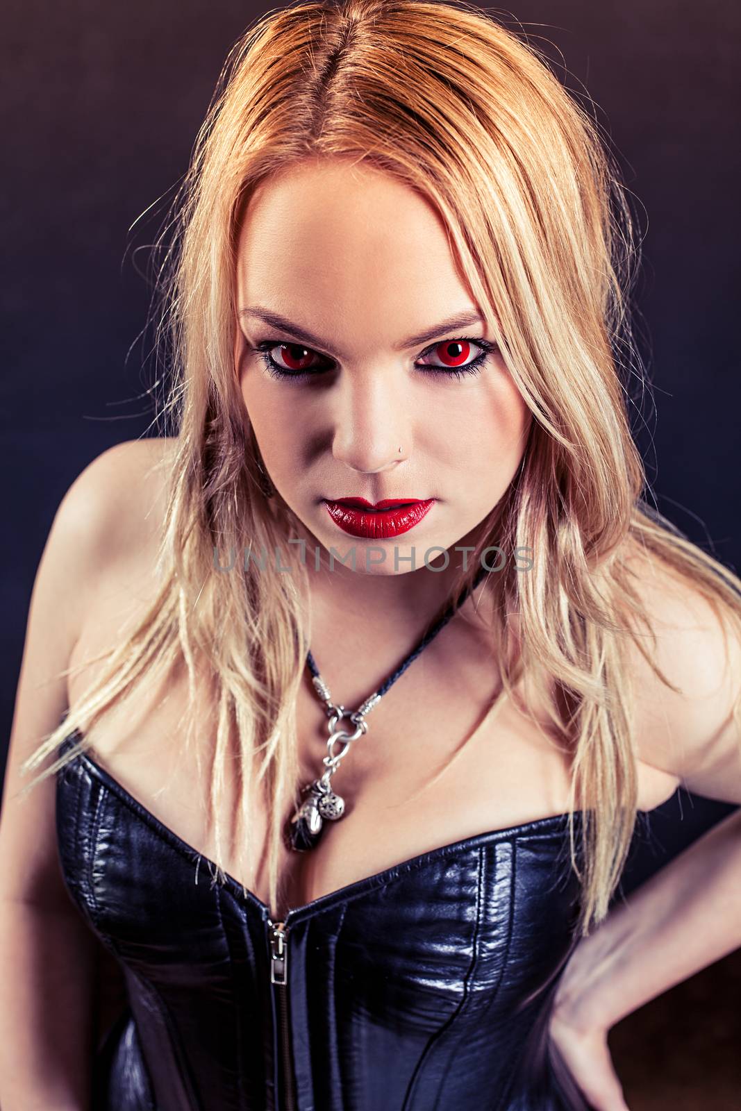 Photo of a woman with red eyes and red lipstick wearing a black leather corset.  Harsh lighting and filtered for scarier feel.