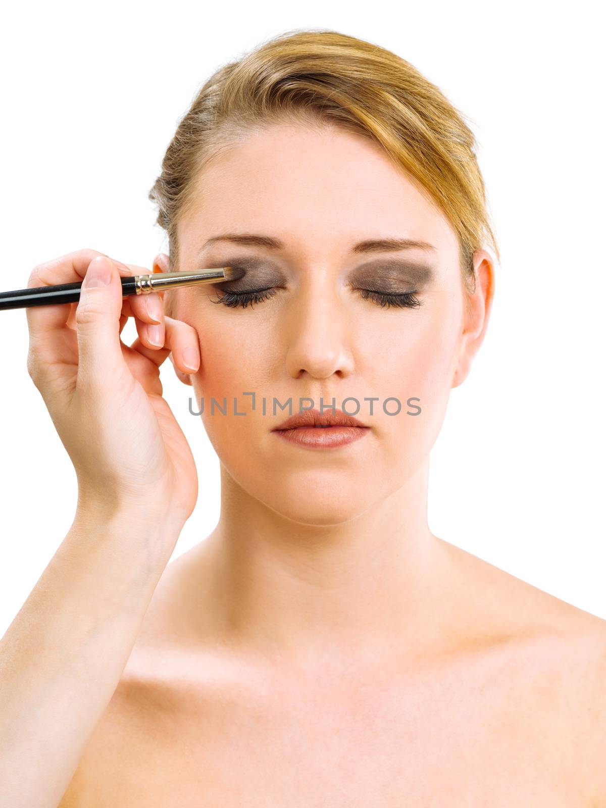 Photo of a makeup artist applying eye makeup onto a blond model.
