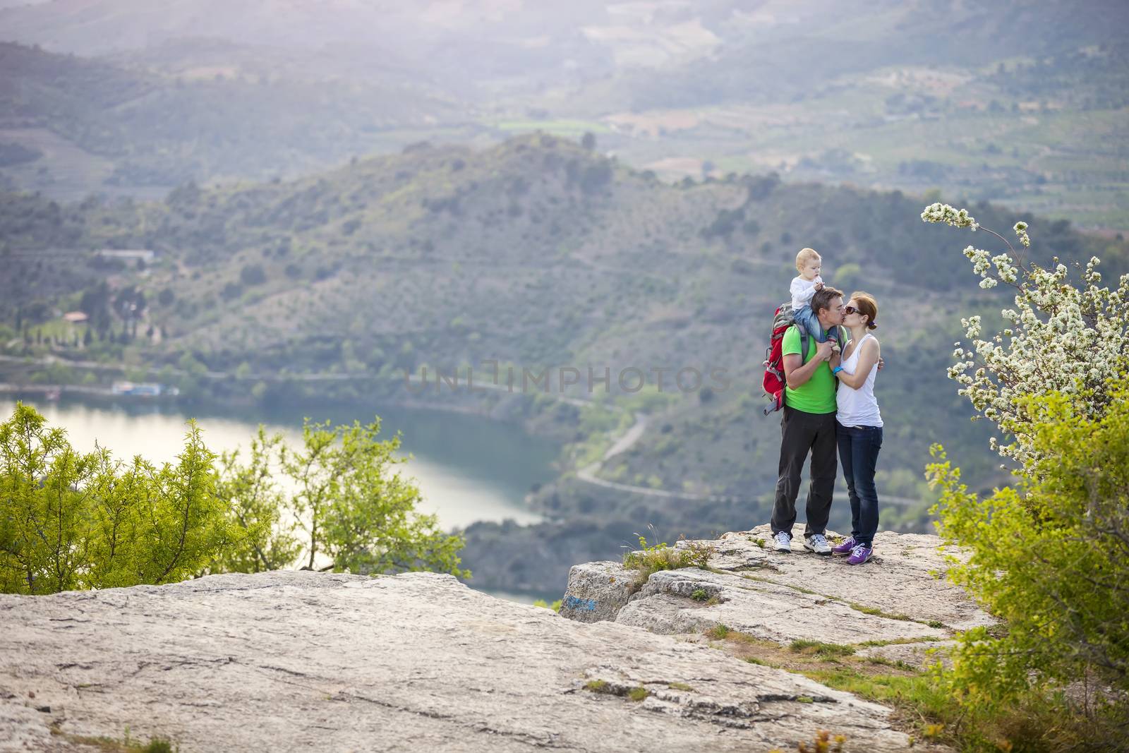 Couple with baby boy standing on cliff and kissing by photobac