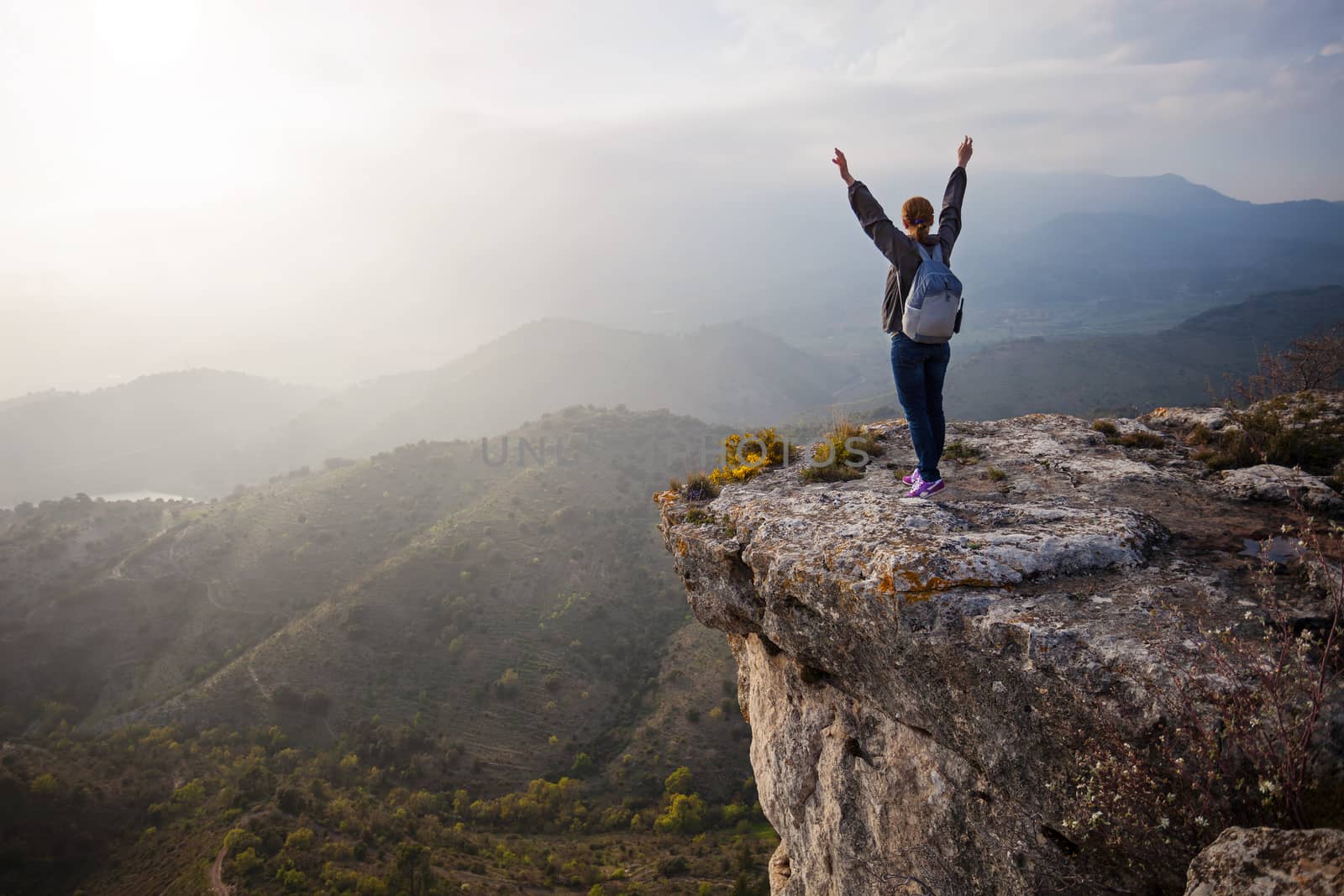 Woman standing on cliff with outstretched arms by photobac
