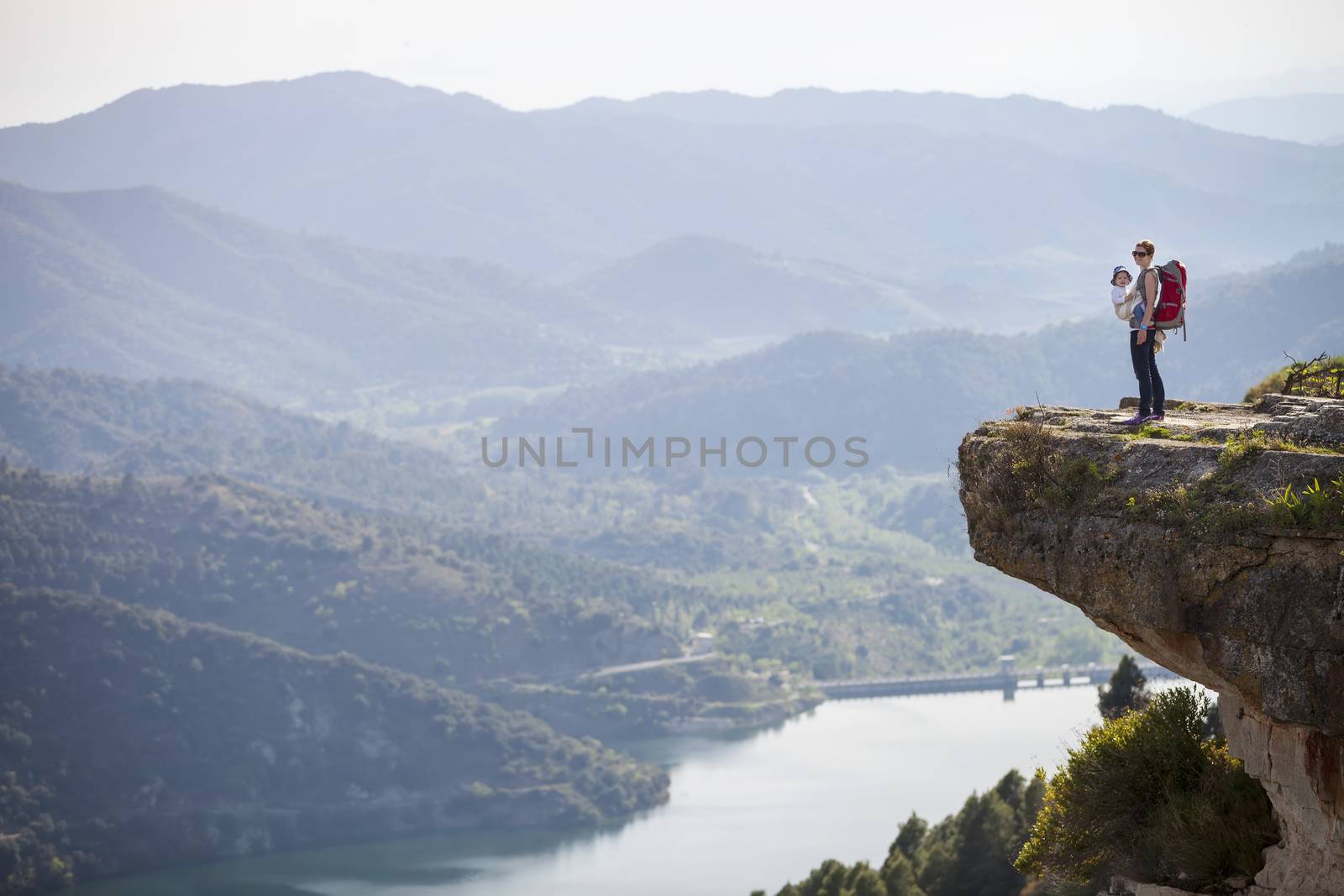 Young mother with baby in sling standing on cliff by photobac