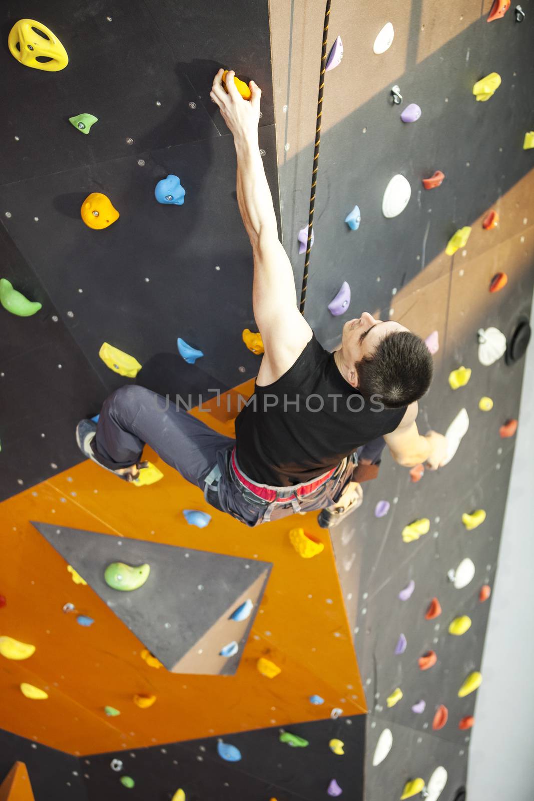 Young man practicing rock-climbing on a rock wall indoors