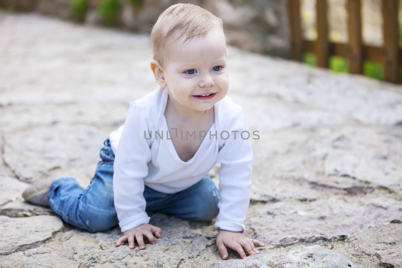 Cute little boy looking up and smiling while crawling on stone paved sidewalk