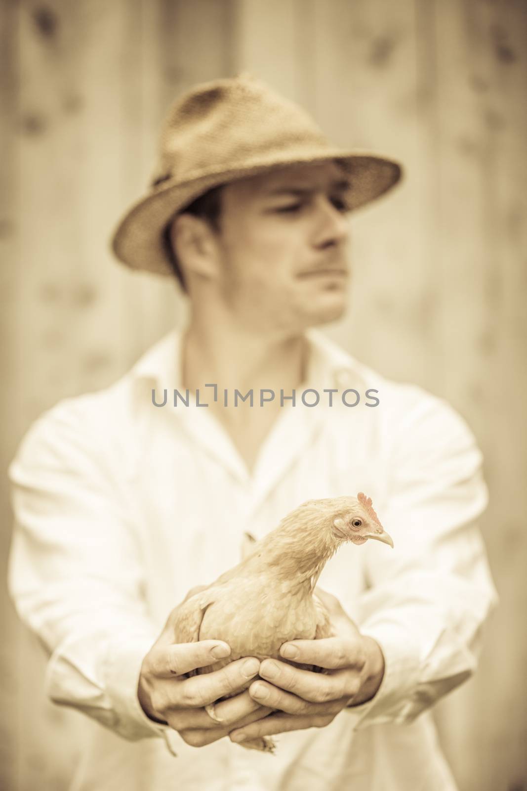 Farmer Holding a Beige Chicken in front of the Farm