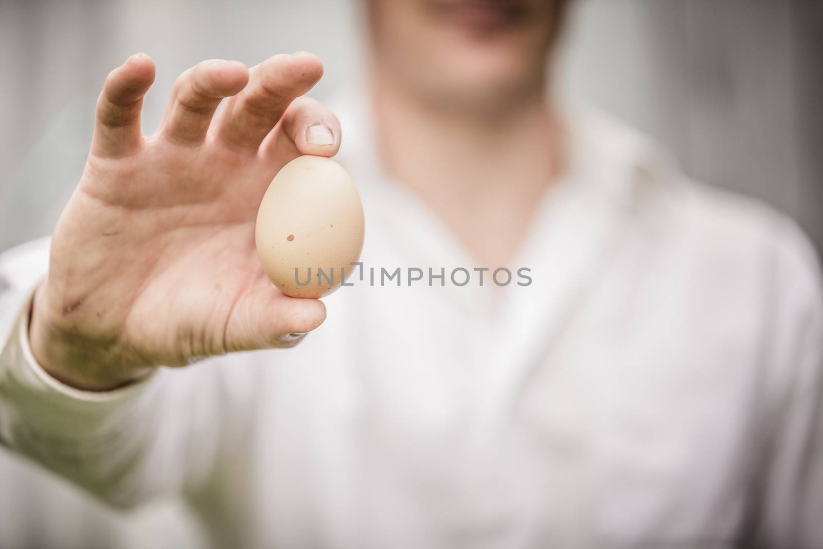 Farmer Showing an Egg in front of the Farm