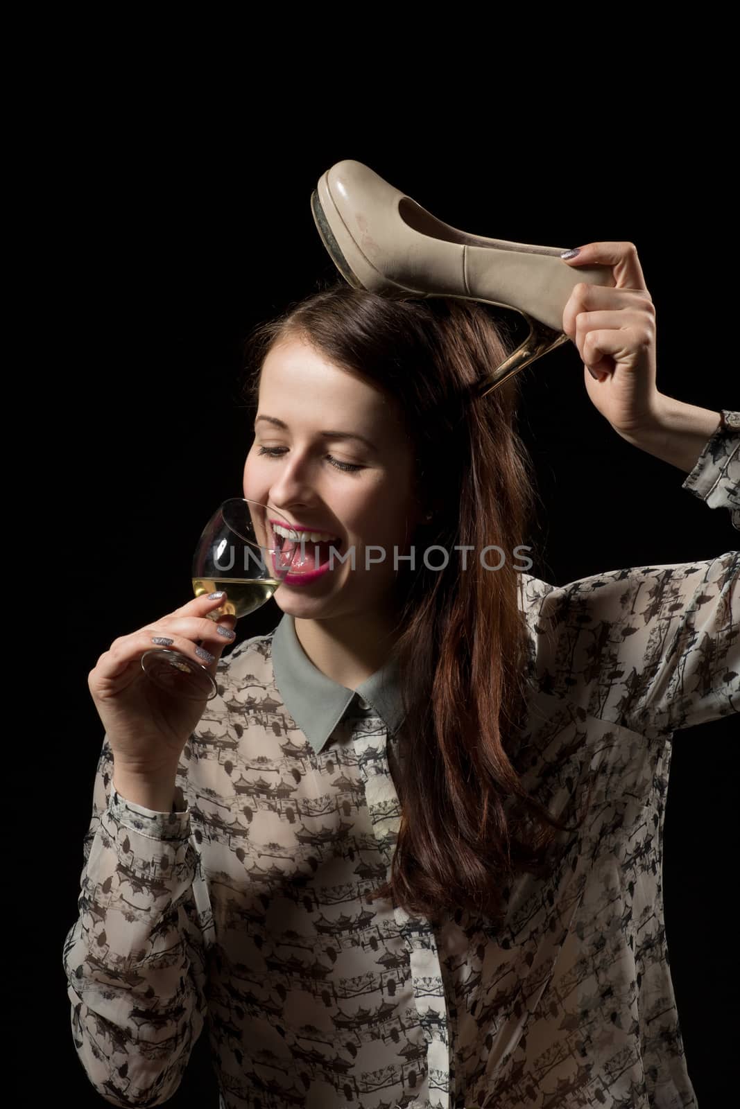 Smiling beautiful young brunette woman holding a glass of white wine and shoe