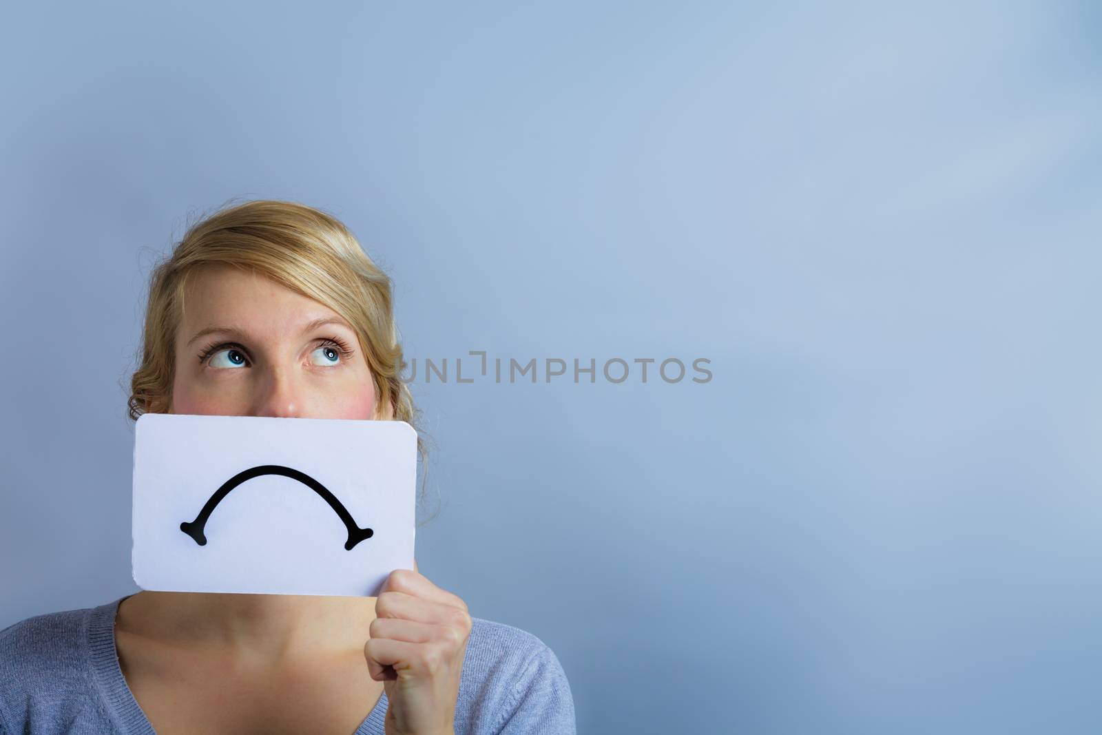 Unhappy Portrait of a Woman Holding a Sad Mood Board with Blue Background