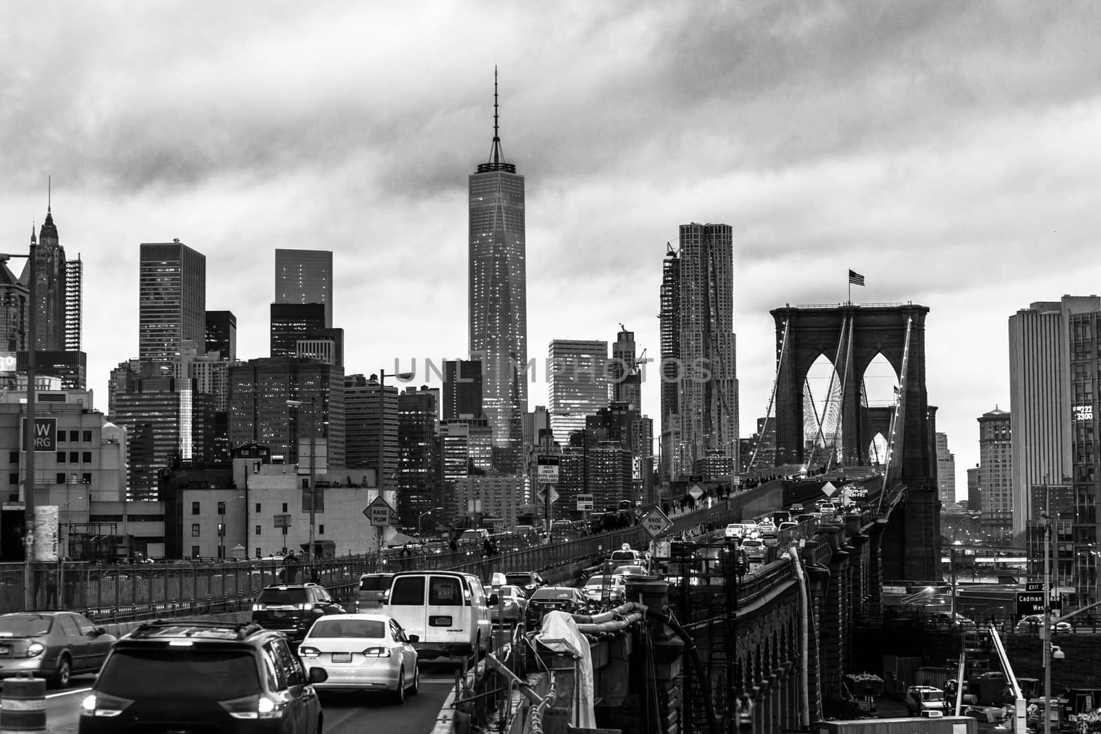 Traffic on Brooklyn bridge and New York City Manhattan downtown skyline at dusk with skyscrapers over East River panorama. Black and white.