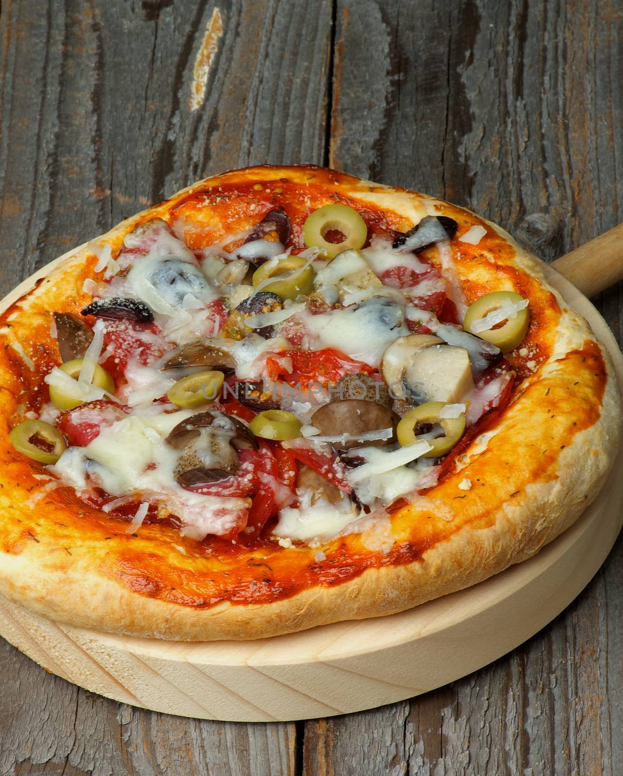 Homemade Pizza Green Olives, Salami, Mushrooms and Grated Cheese on Circle Cutting Board closeup on Wooden background
