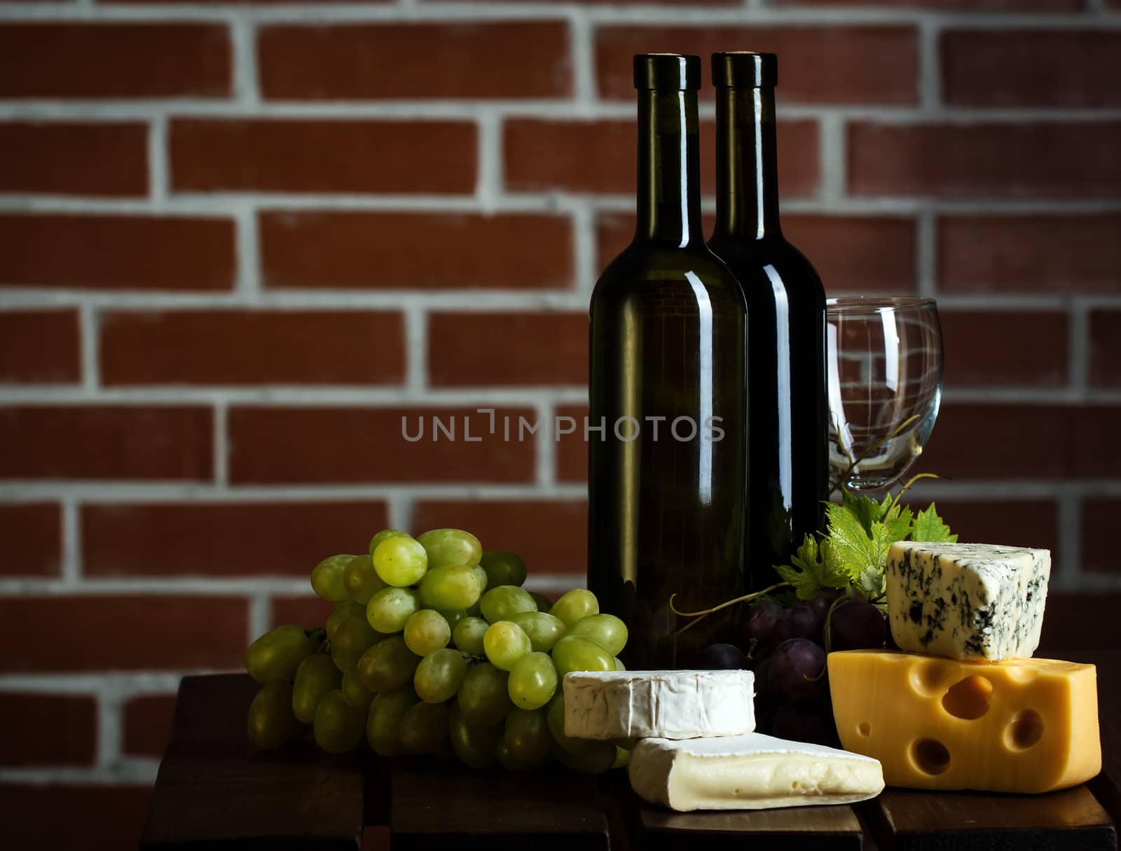 Wine bottles with grape and cheese on brick wall background