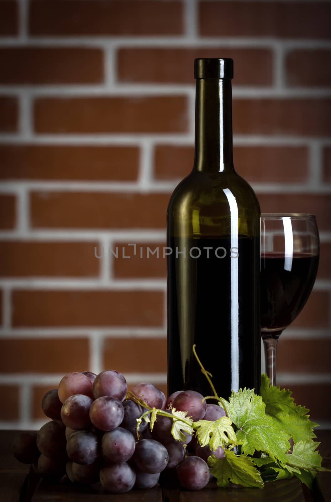 Red wine bottle with glass and grape on brick wall background