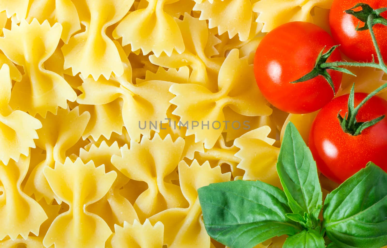 Raw farfalle pasta background with cherry tomato and basil leaf