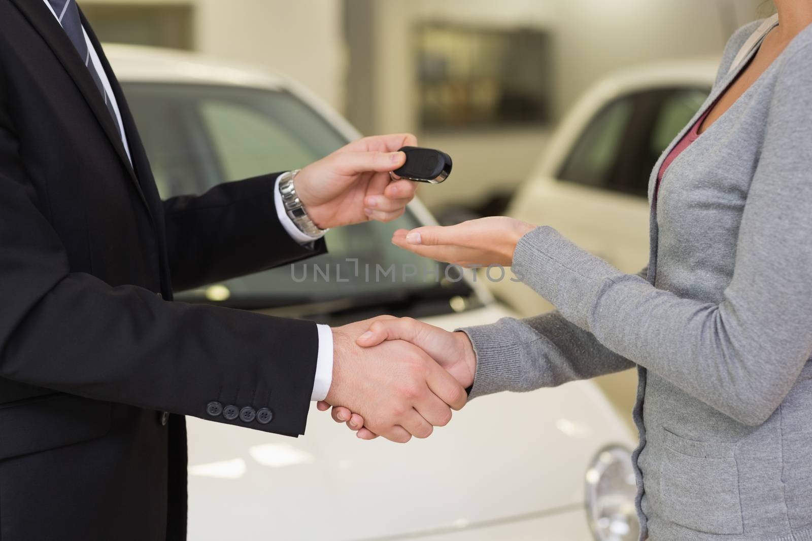 Businessman giving car key while shaking a customer hand at new car showroom