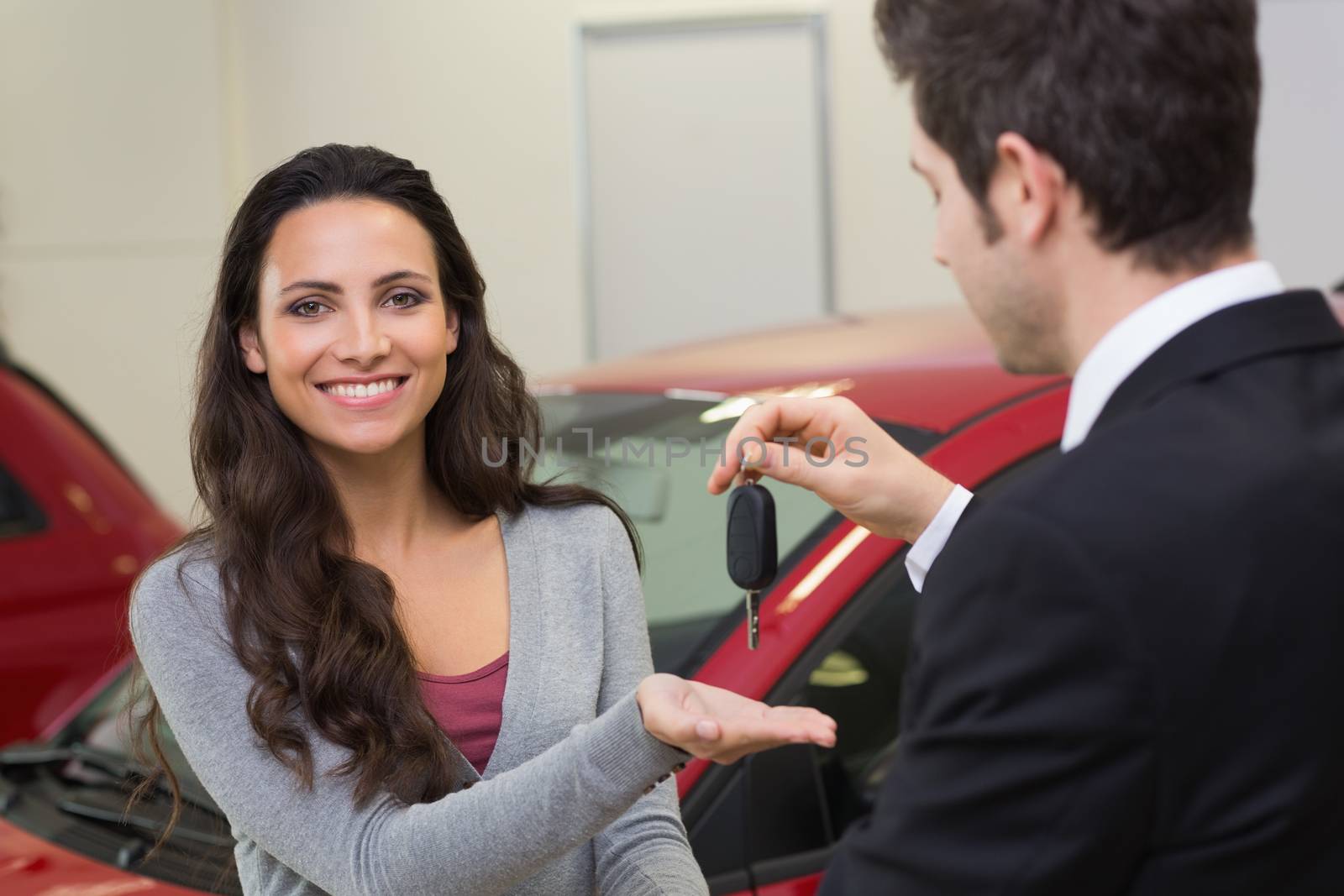 Businessman giving car key while shaking a customer hand at new car showroom