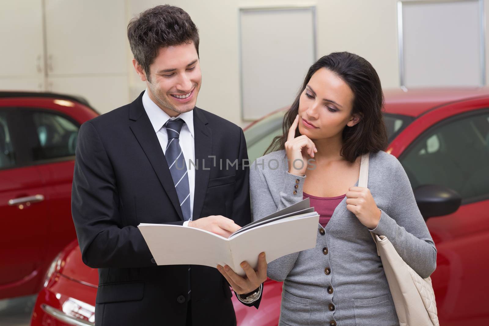 Salesman showing brochure to customer and smiling at new car showroom
