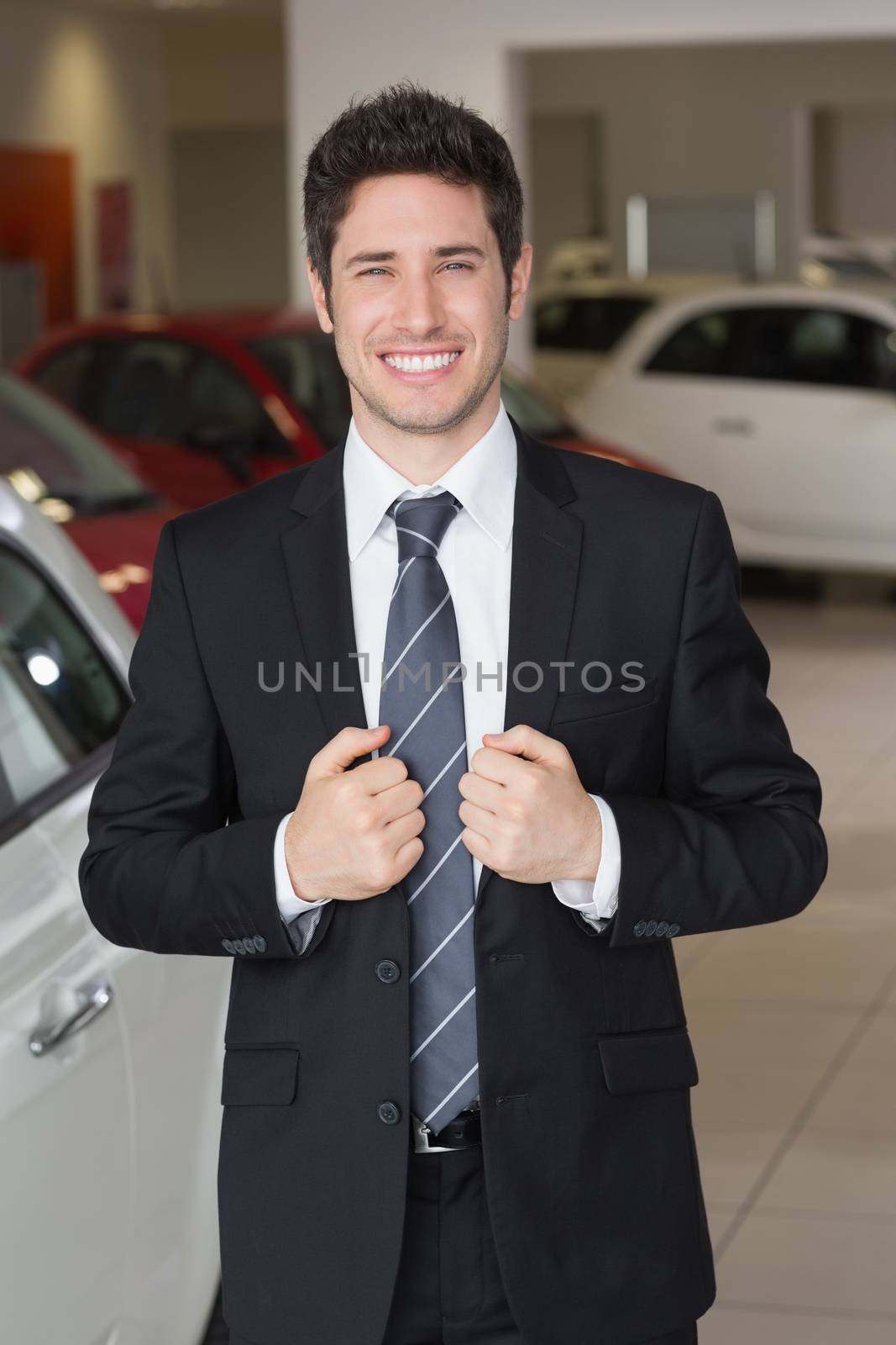 Handsome businessman in suit stading at new car showroom