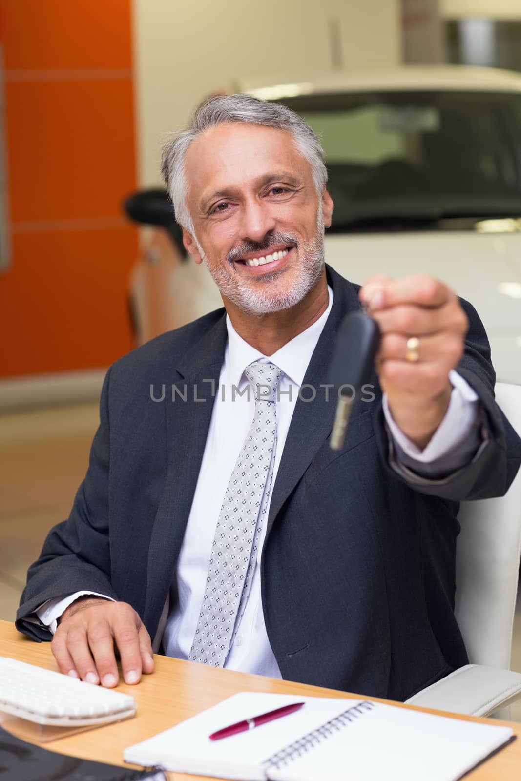 Smiling salesman giving a customer car keys at new car showroom
