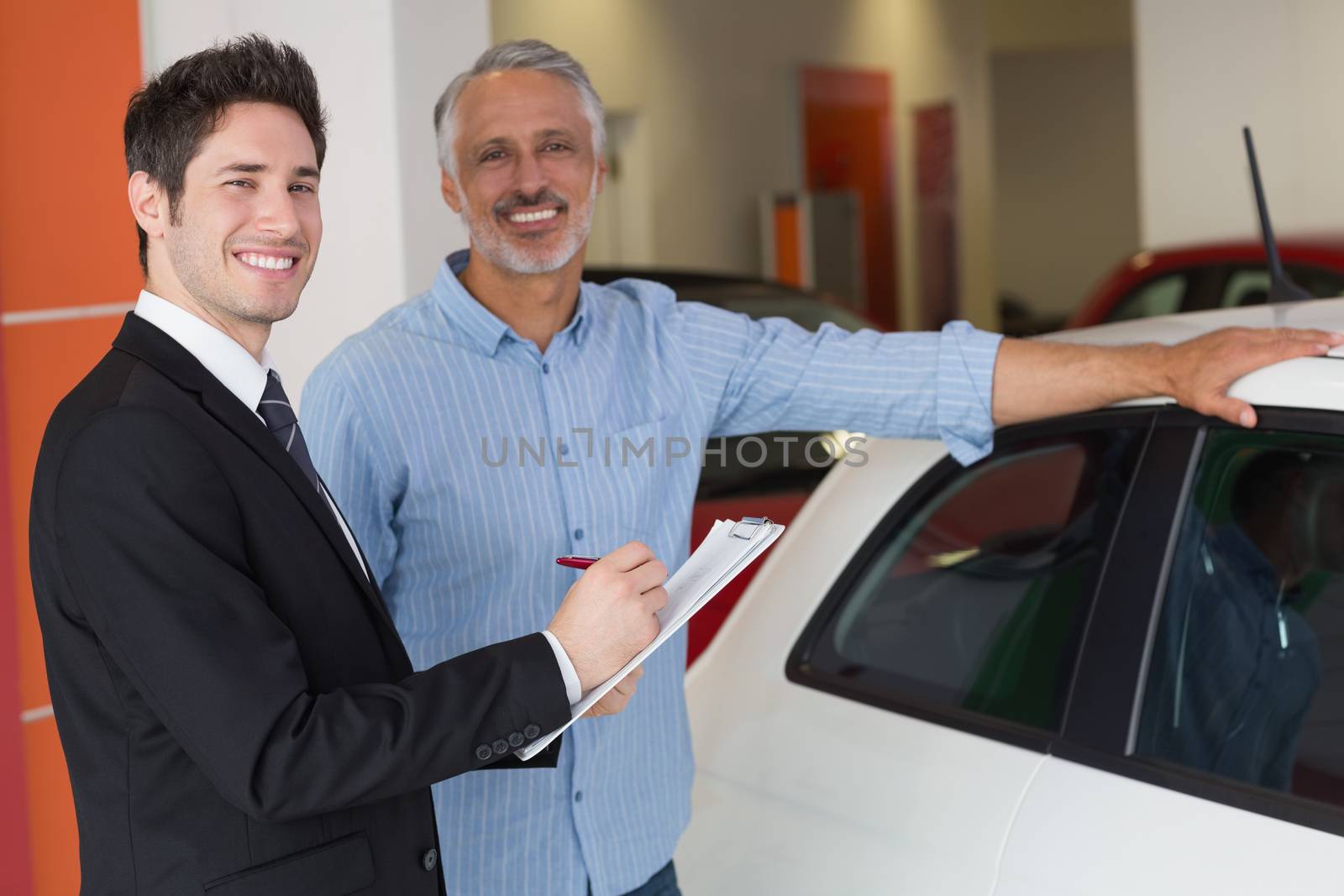 Smiling businessman writing on clipboard at new car showroom