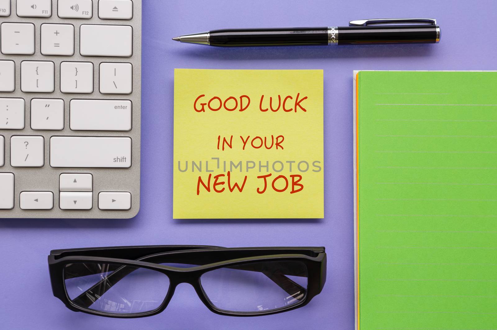 Top view of yellow notepad with words " Good Luck In Your New Job " putting on workspace with pen, keyboard, paper book and glasses sort orderly