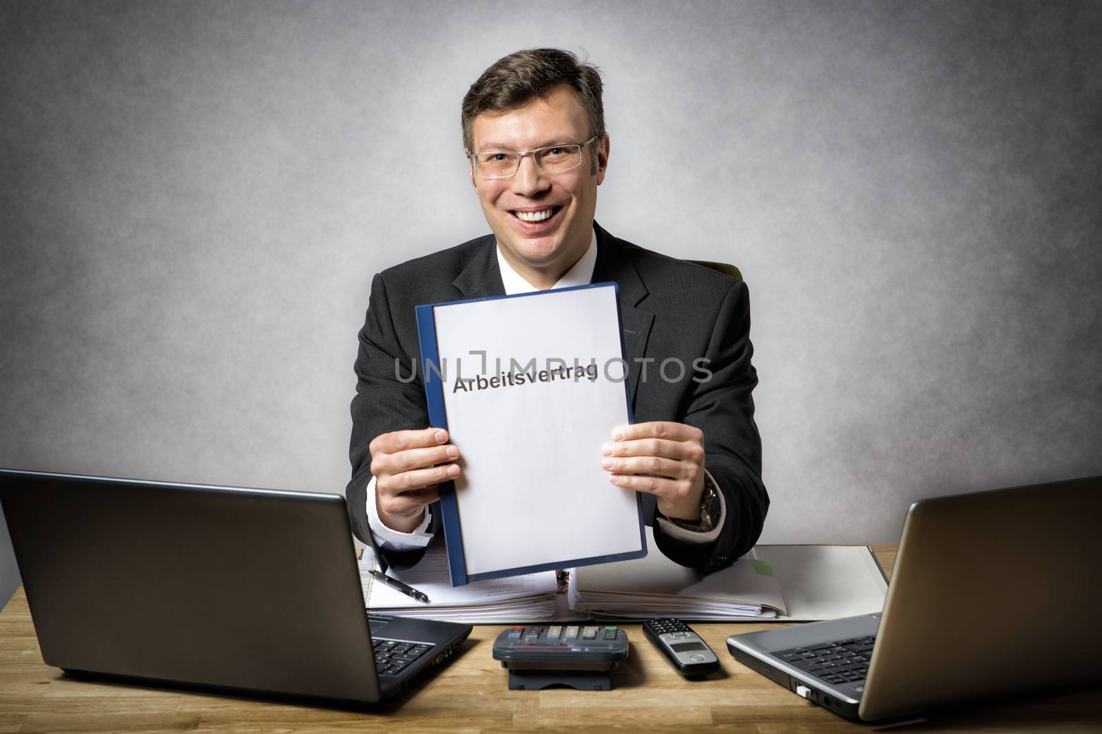 Businessman at the office desk is holding a employment contract with german title "Arbeitsvertrag"