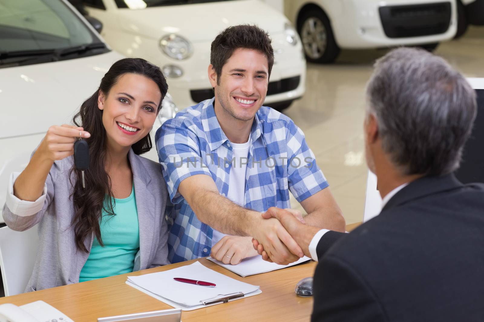 Salesman giving car keys to a couple at new car showroom