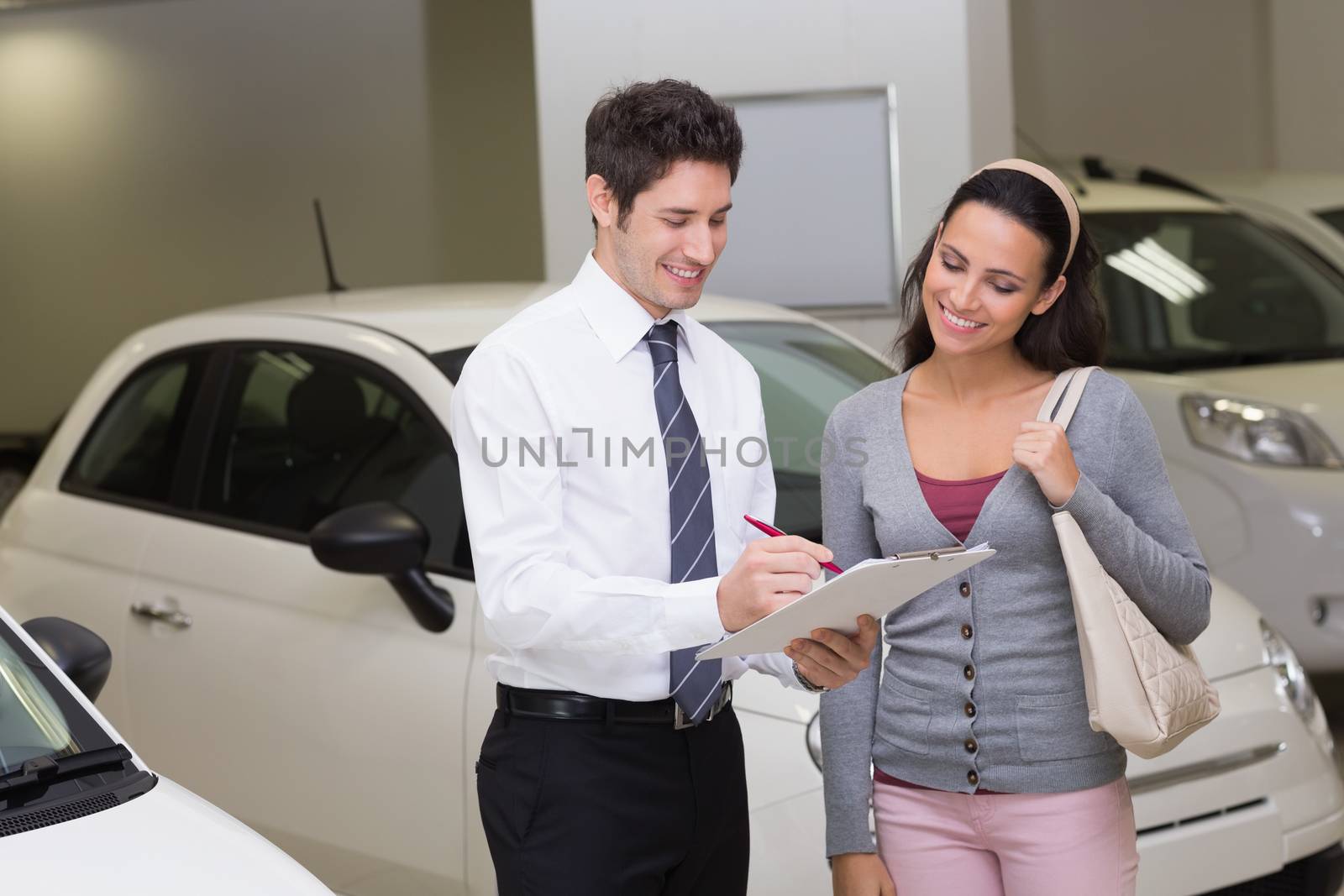 Salesperson showing clipboard to sign to customer at new car showroom