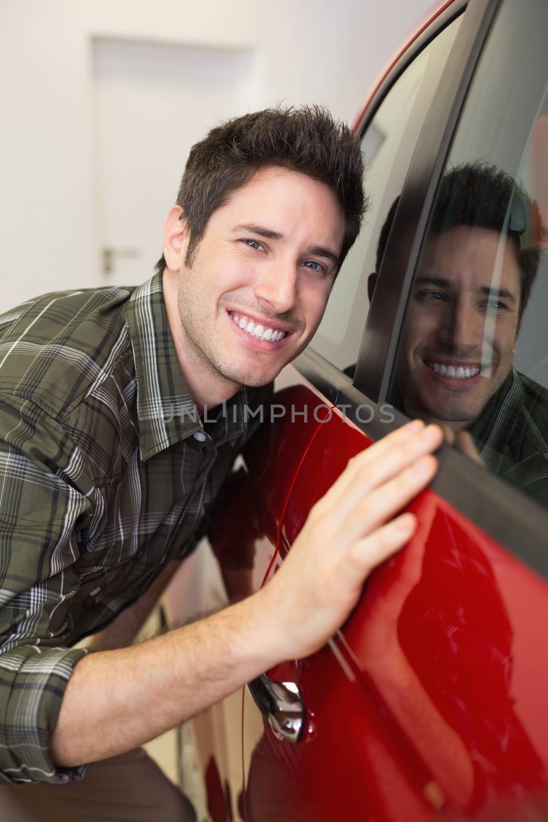 Smiling man hugging a red car by Wavebreakmedia
