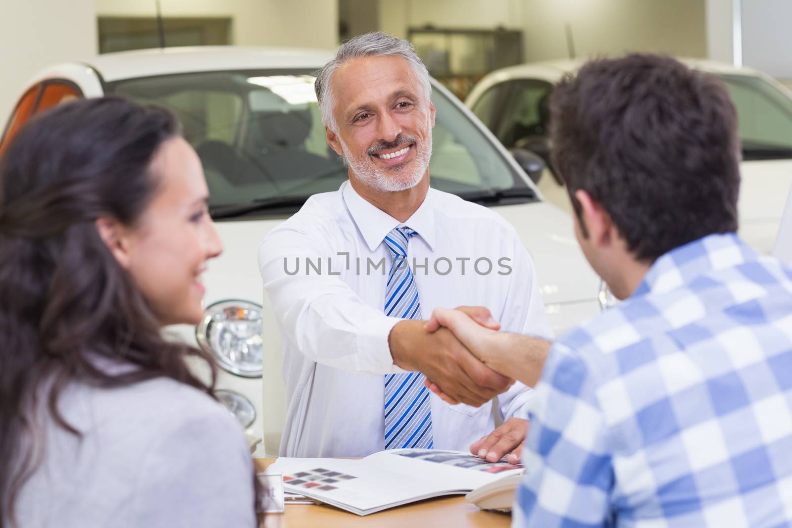 Smiling salesman shaking a customer hand at new car showroom