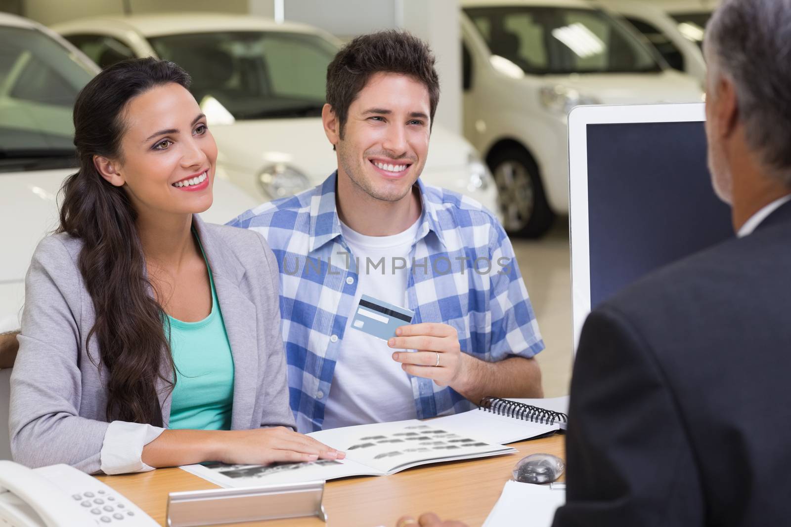 Smiling couple holding credit card to buy a car at new car showroom