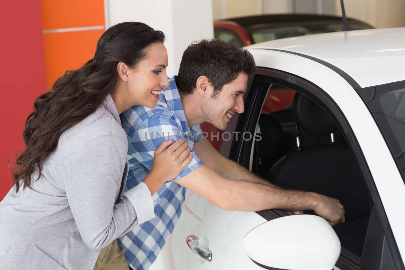 Smiling couple looking inside a car at new car showroom