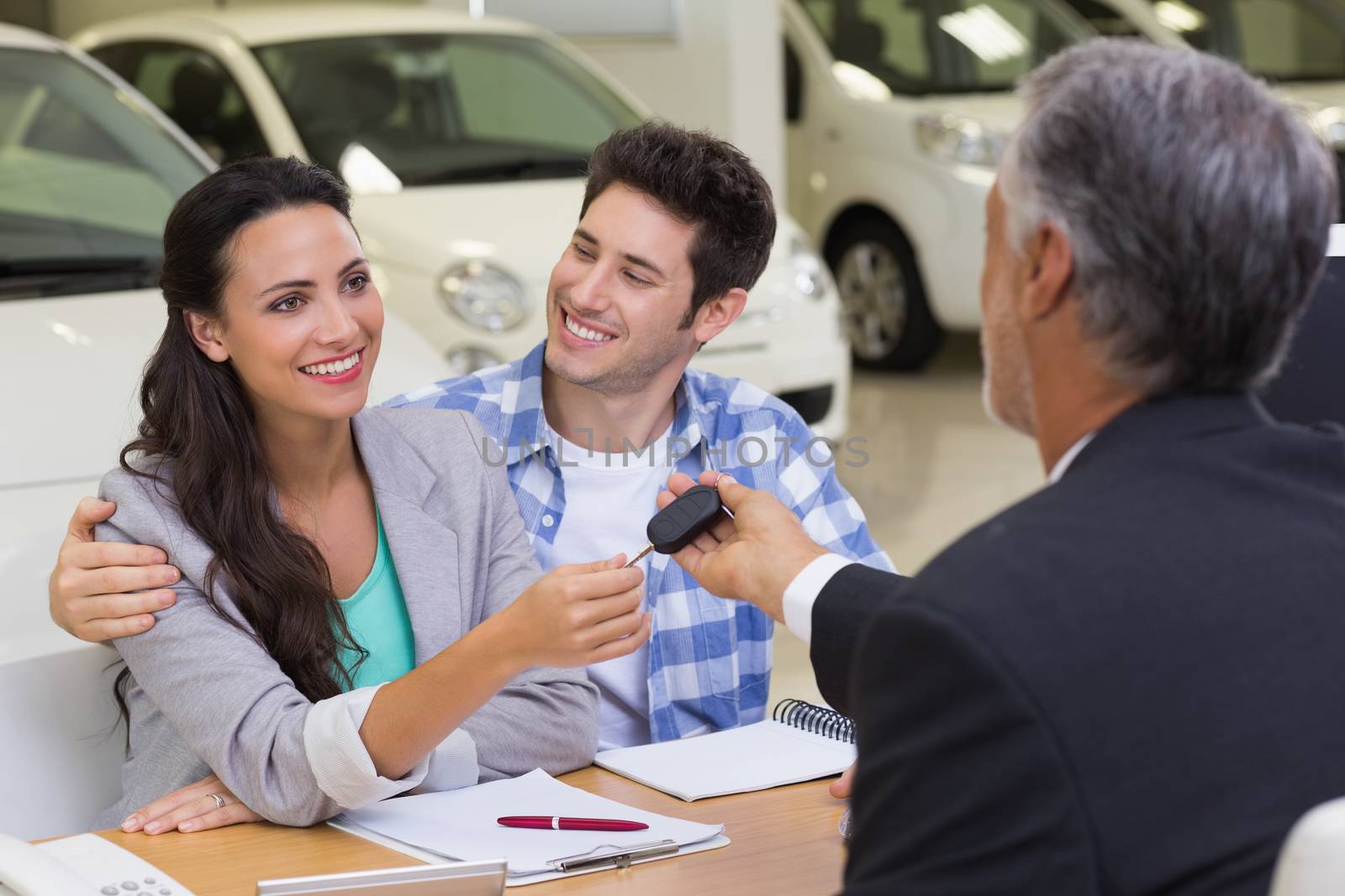 Salesman giving car keys to a couple at new car showroom