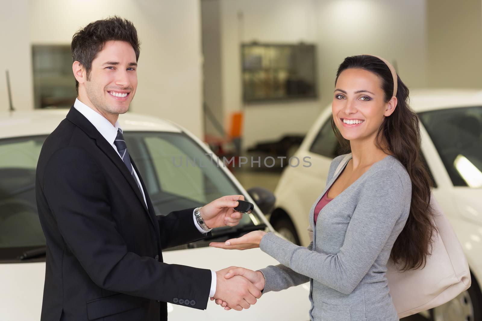 Businessman giving car key while shaking a customer hand at new car showroom