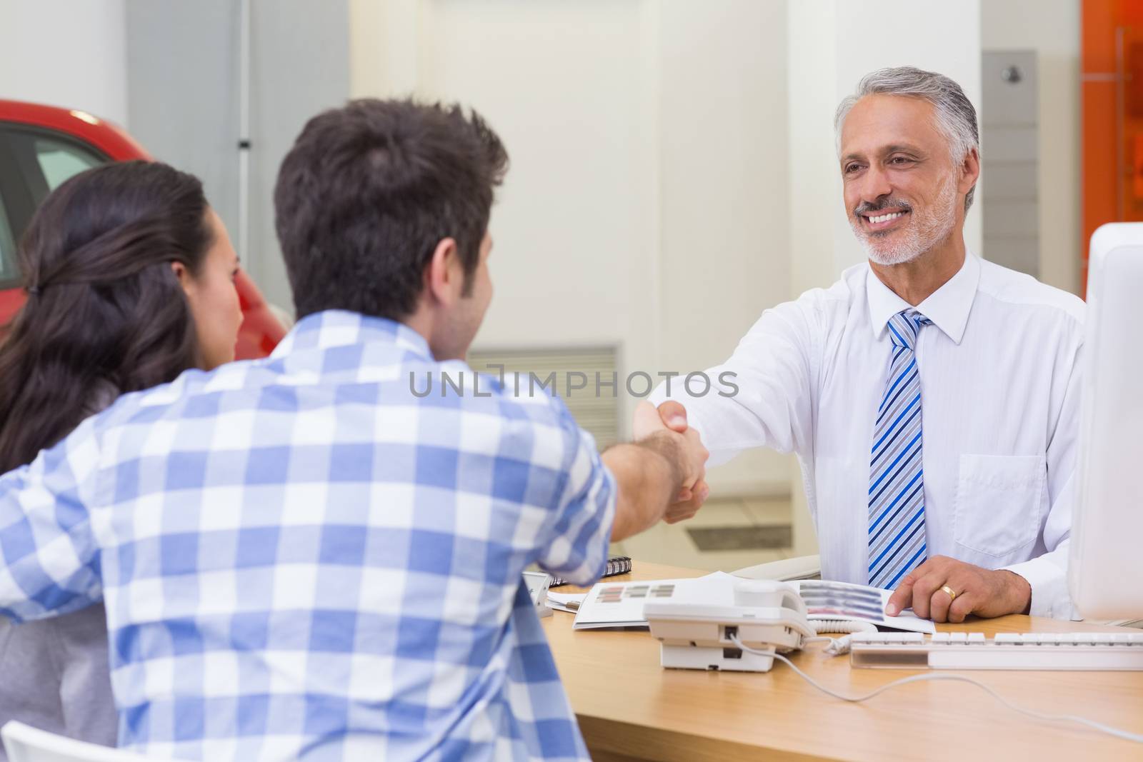 Smiling salesman shaking a customer hand at new car showroom