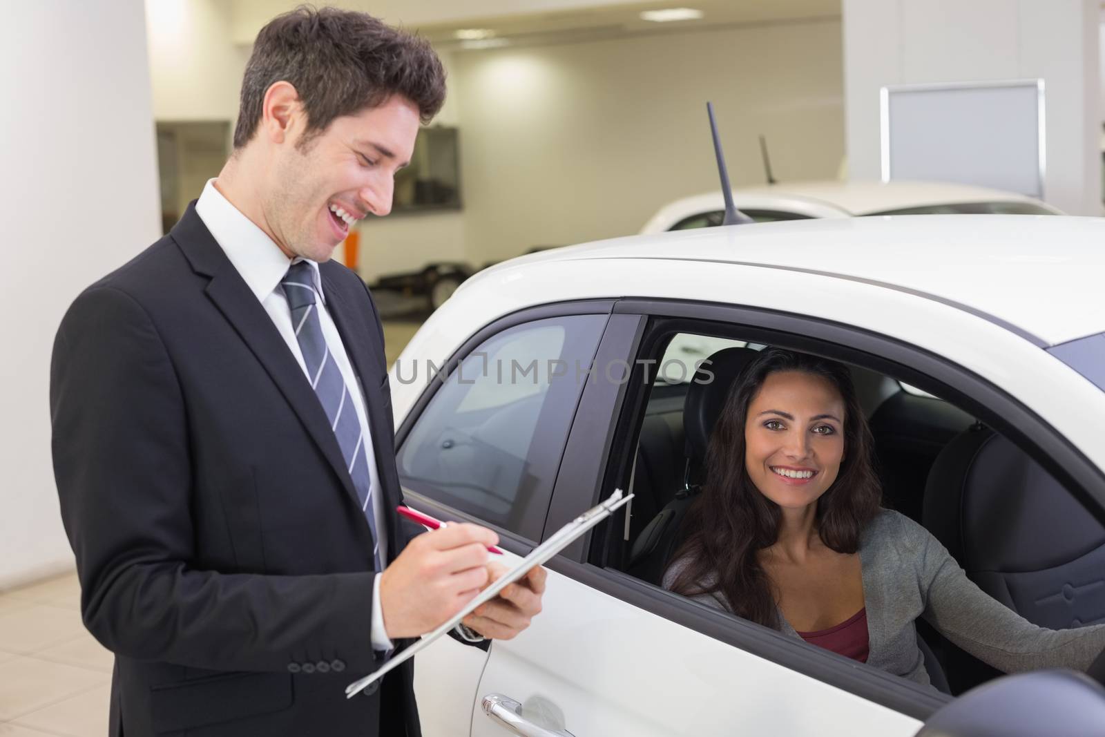 Smiling businessman writing on clipboard at new car showroom