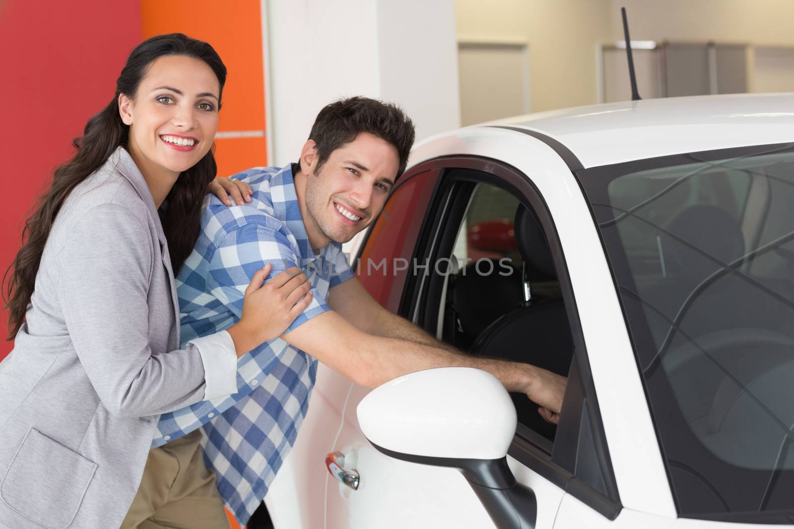 Smiling couple looking inside a car at new car showroom