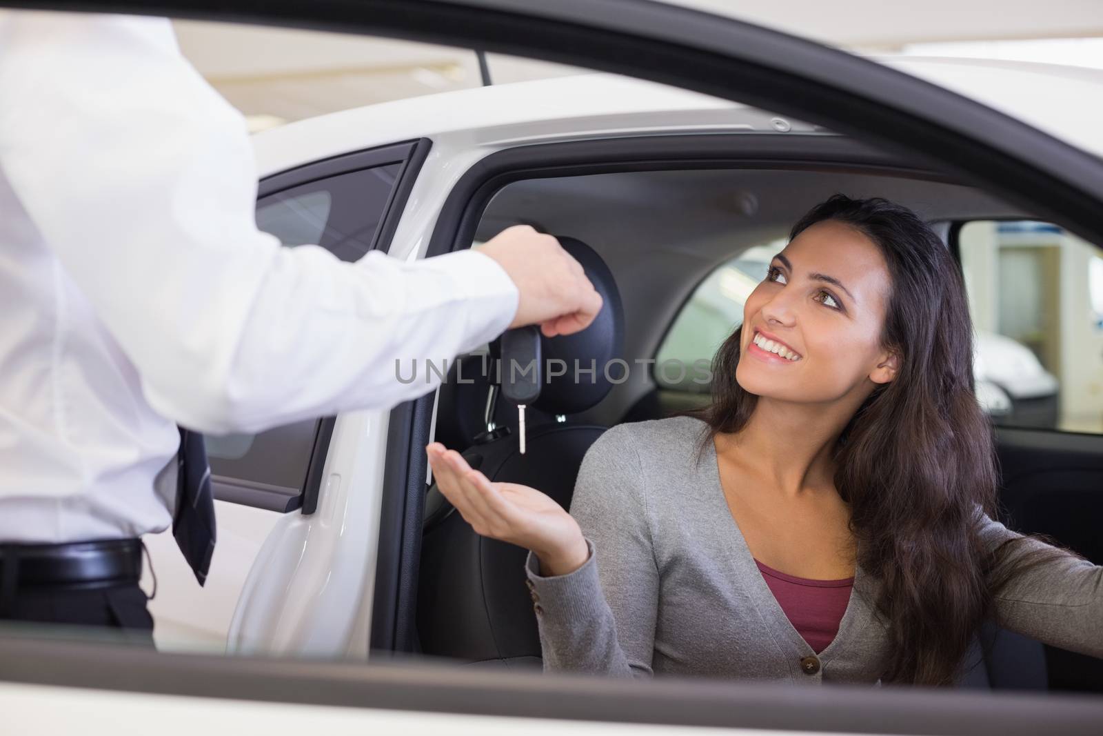 Salesman giving keys to a smiling woman at new car showroom