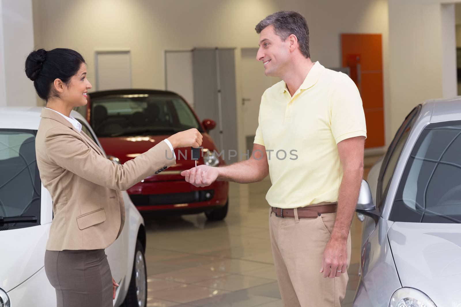 Smiling businesswoman giving car key to happy customer at new car showroom