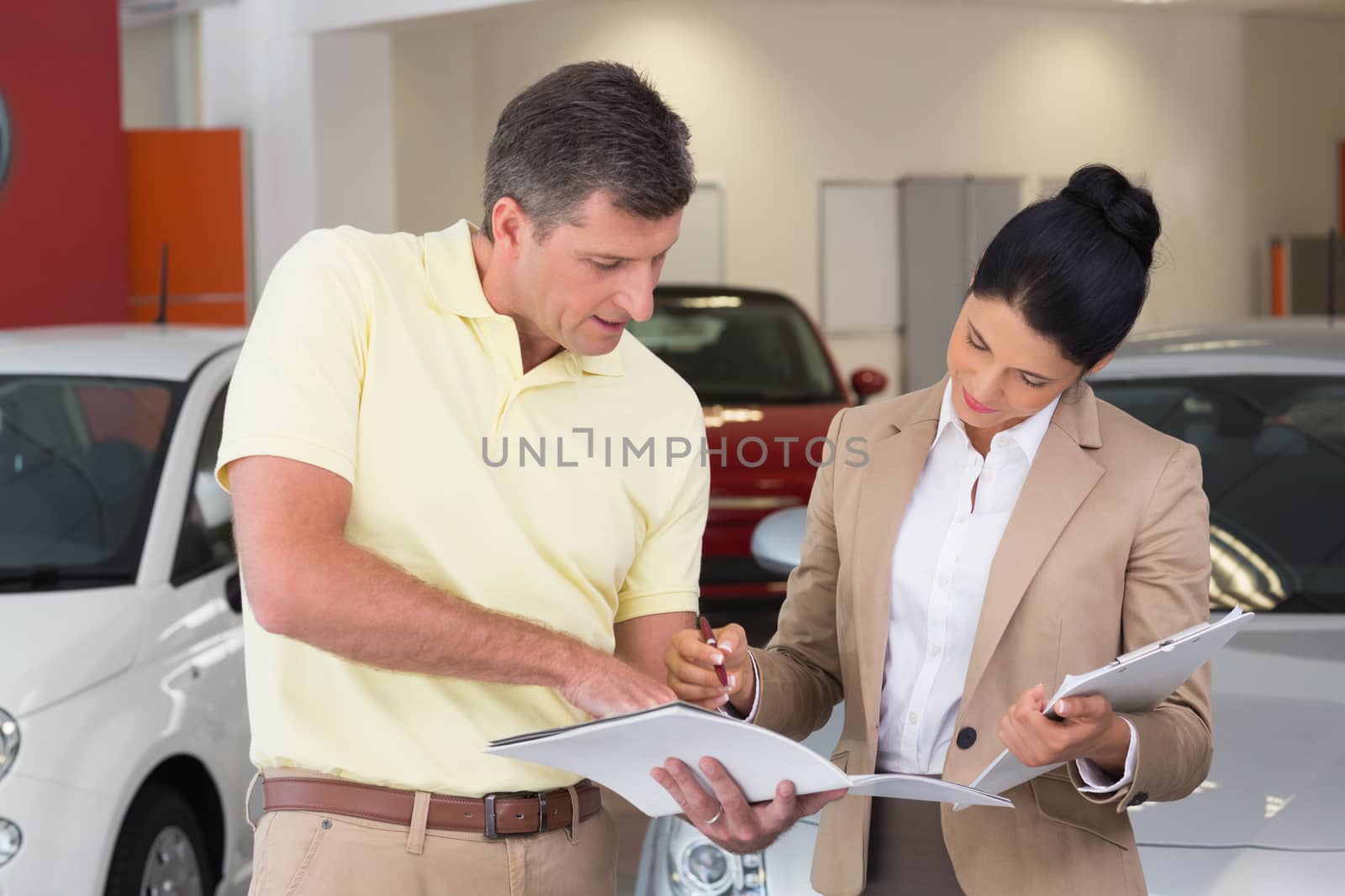 Salesperson talking with her customer while holding a booket at new car showroom