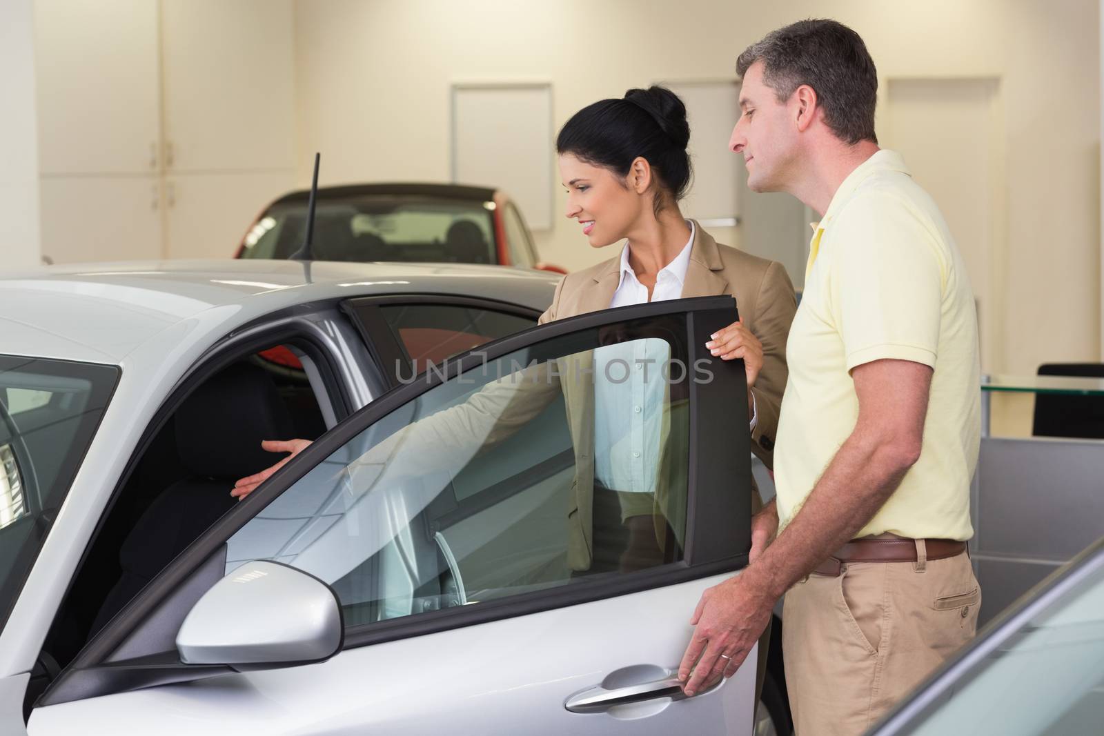 Businesswoman showing a car interior to her customers at new car showroom