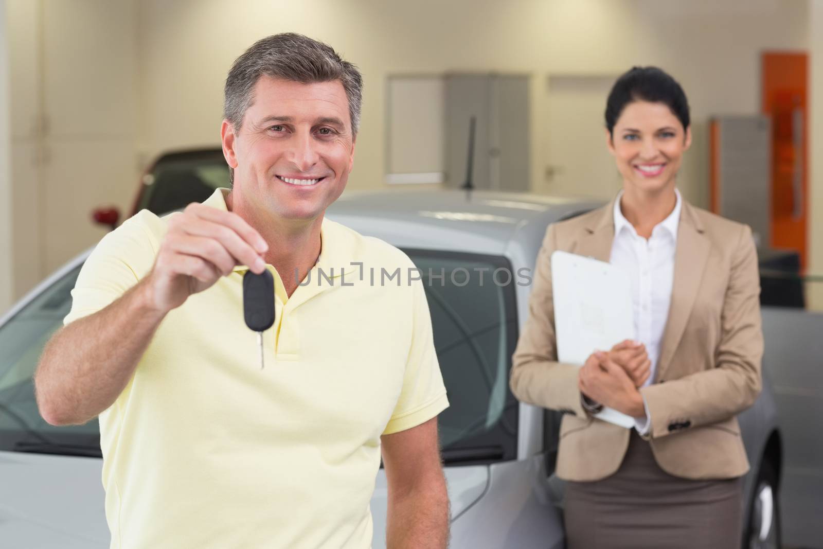 Smiling customer showing his new car key at new car showroom