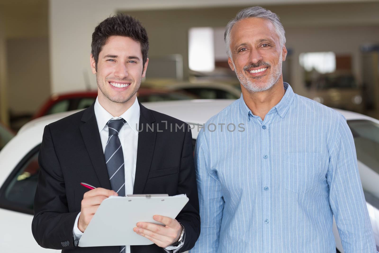 Smiling businessman writing on clipboard by Wavebreakmedia