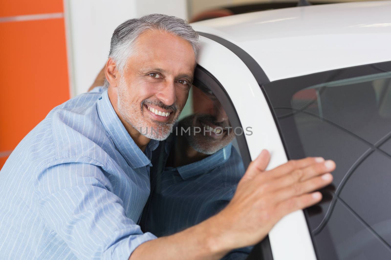 Smiling man hugging a white car at new car showroom