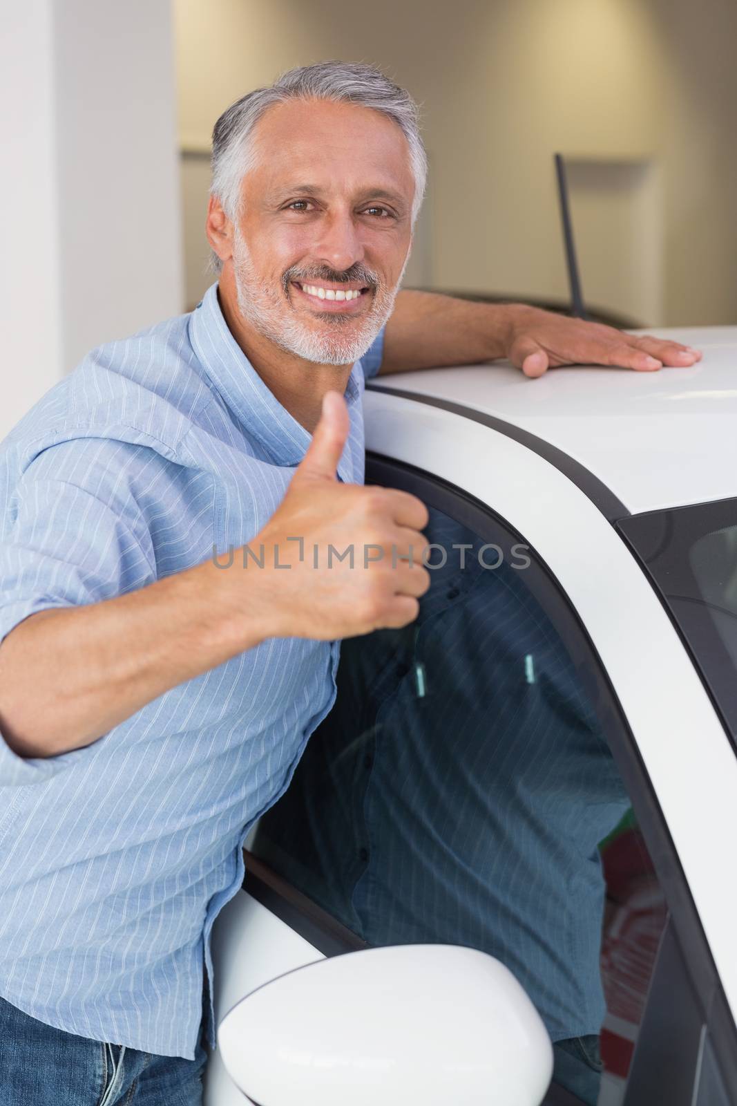 Smiling man hugging a white car while giving thumbs up by Wavebreakmedia