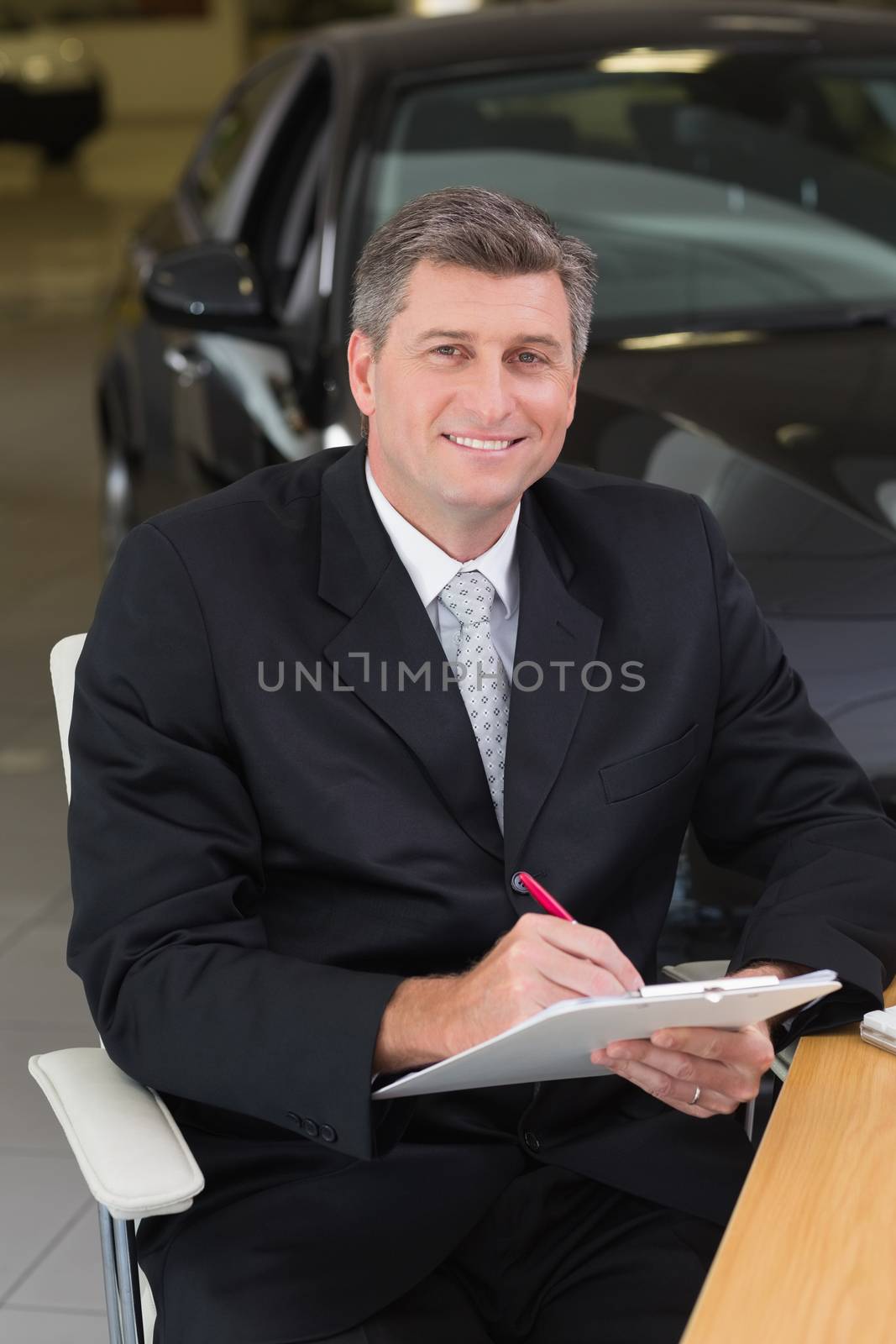 Businessman sitting at his desk while writing on clipboard by Wavebreakmedia