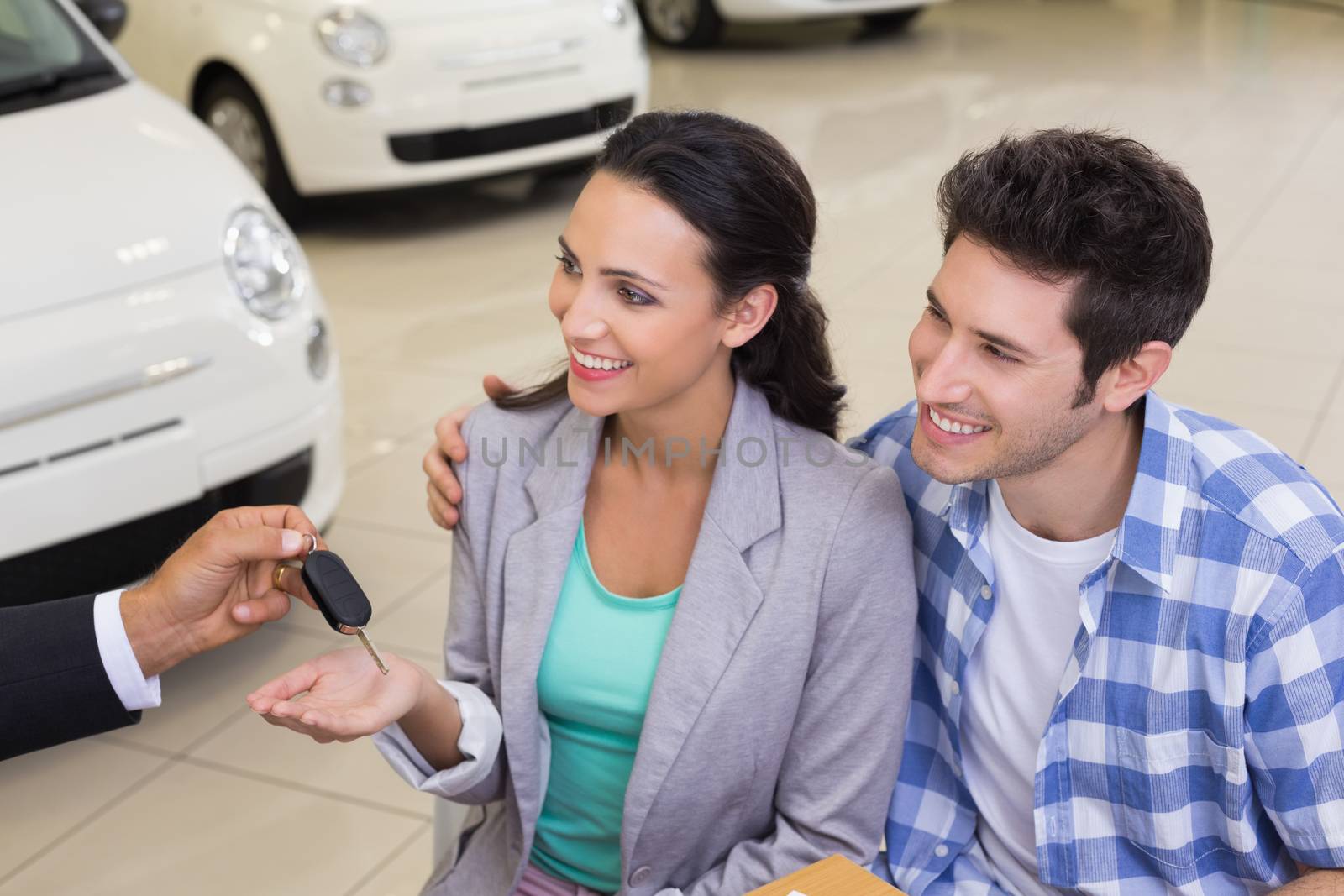 Smiling young couple receiving key at new car showroom