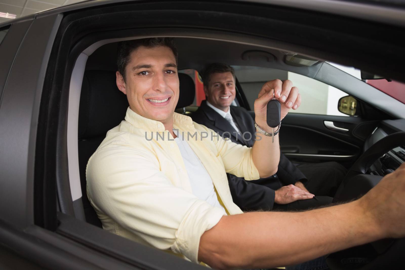 Happy male driver at the wheel sitting in his car at new car showroom