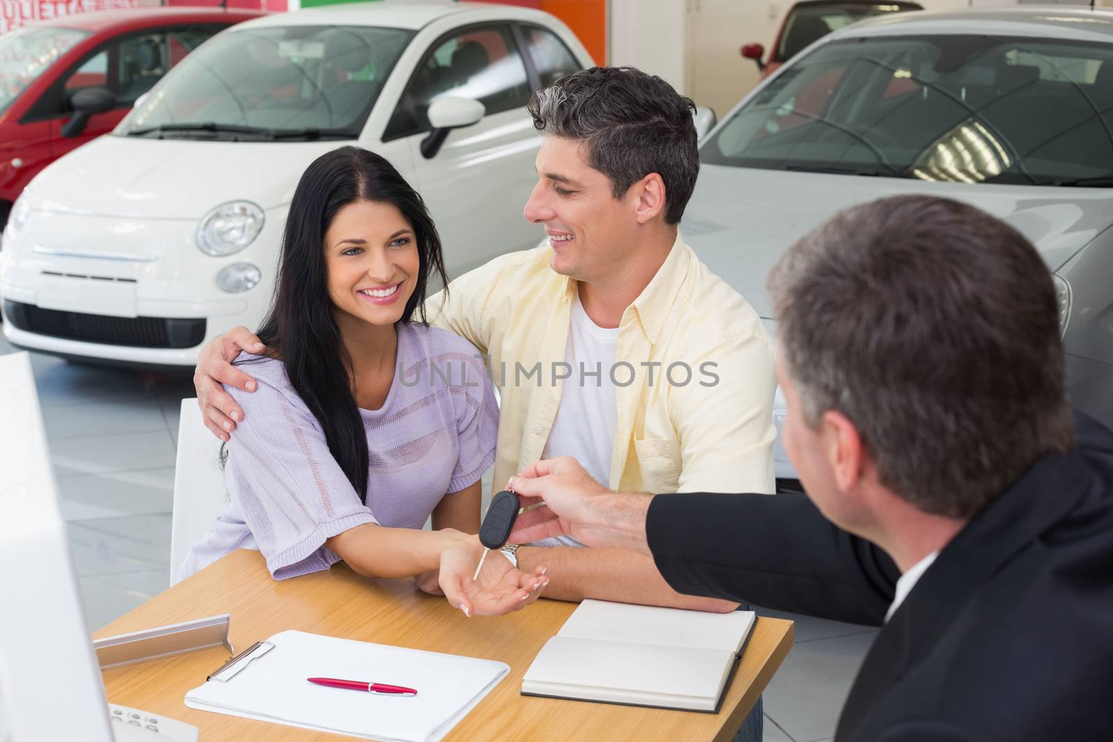 Salesman giving key to a smiling couple at new car showroom