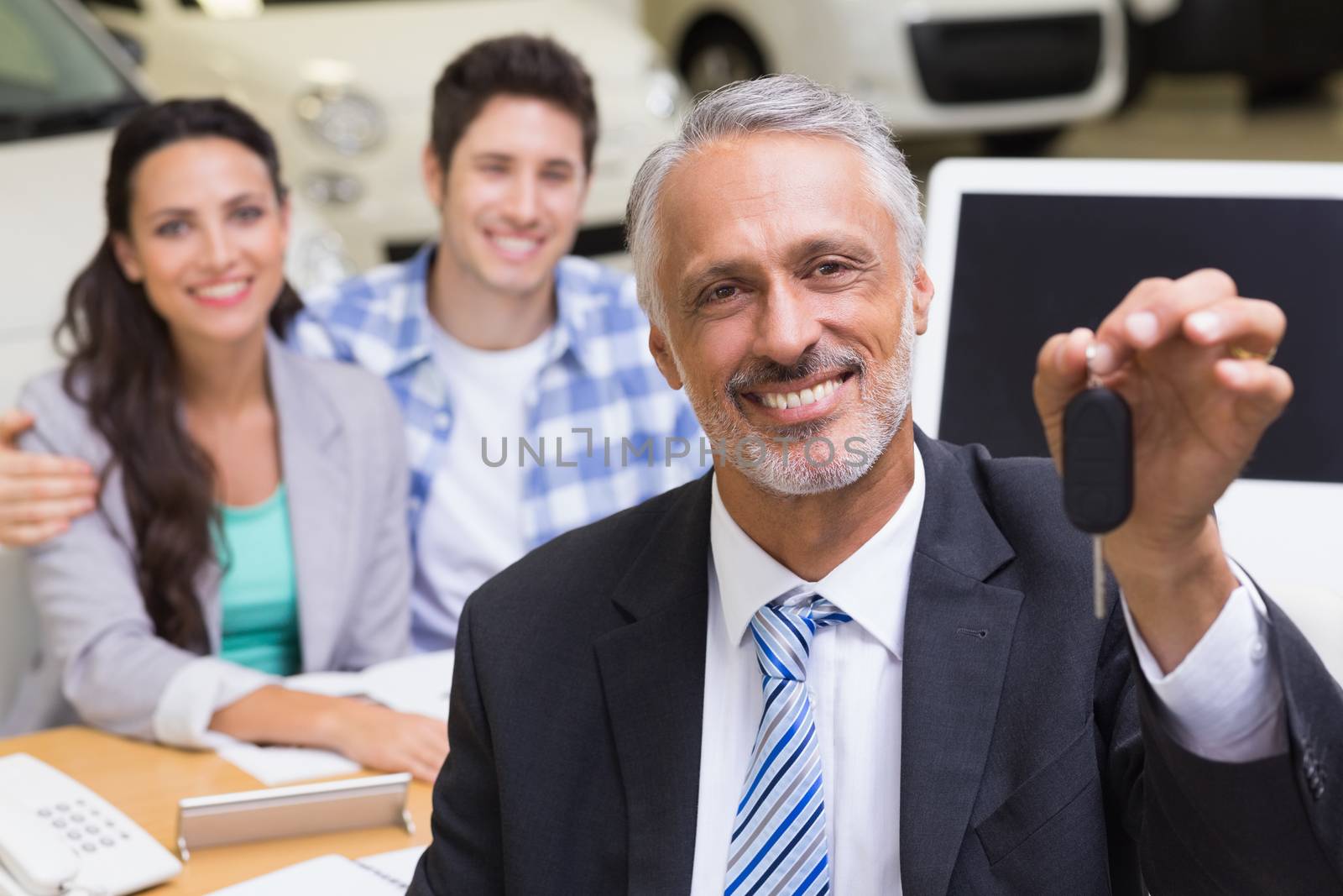 Smiling businessman showing a car key at new car showroom