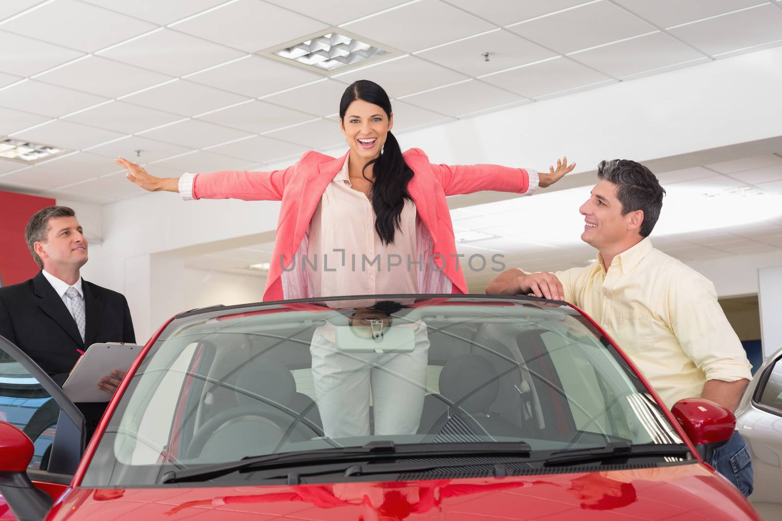 Woman having fun in her new red convertible at new car showroom